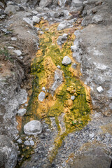 Sulfur hot spring flowing from the Himalayas with green-yellow mineral markings on stones and rising steam, showcasing geothermal activity, Himalayan landscape, and natural wonder
