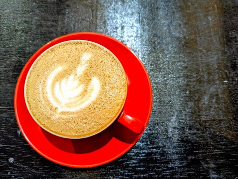 Cappuccino with latte art on a red saucer sitting on a dark table - Powered by Adobe
