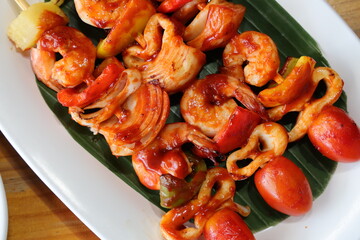 Grilled Shrimp Skewers: A vibrant arrangement of grilled shrimp skewers presented on a white plate and fresh green leaf, showcasing succulent seafood and colorful vegetables.