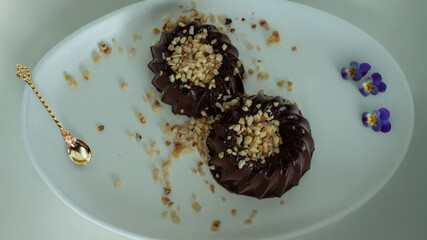 Two chocolate jellies topped with chopped nuts on a white plate, decorated with edible flowers.