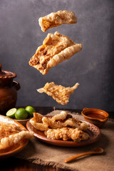 Pork rinds falling on a dish. Chicharron. Crispy pork skin pieces, traditional mexican ingredient or snack served with lemon juice and red hot chili sauce.