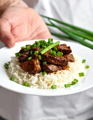Savory stir-fried meat and rice dish topped with fresh green onions, presented on a white plate.