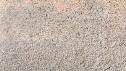 A close-up shot of a light beige, rough texture. The surface appears uneven and granular, with subtle color variations creating a tactile feel.