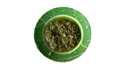 Sambal ljo on a green leaf plate, presented on a white background. The chili sauce is in a bowl, showcasing its vibrant green color and texture.