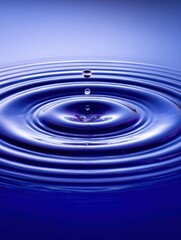 Close-up of water droplet falling into a calm water surface creating ripples and concentric circles with a blue background