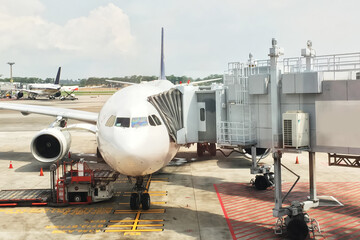 A commercial airplane parked at an airport gate with jet bridge connect show front view, engine and cockpit include ground support equipment under a cloudy summer sky environment.