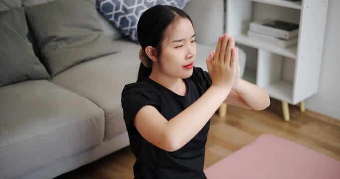 Handheld high angle view shot, Calm Asian woman is enjoying yoga in lotus position on a yoga mat in living room at home. Healthy Lifestyle Concepts