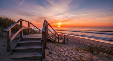 Obraz premium Wooden stairs leading down to a serene beach at sunrise, showcasing warm colors and a tranquil atmosphere.