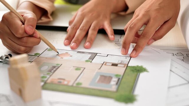 Professional engineer team discussion about house design on meeting table with architectural equipment and building blueprint scatter around at modern office. Focus on hand. Closeup. Delineation.