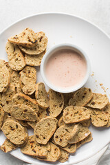 overhead view of slices of savory biscotti with dip, top view of thinly sliced bread chips with sauce, top view of crostini bread slices on marble countertop