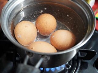 Fresh brown eggs gently boiling in a stainless steel pot on a gas stove creating healthy breakfast