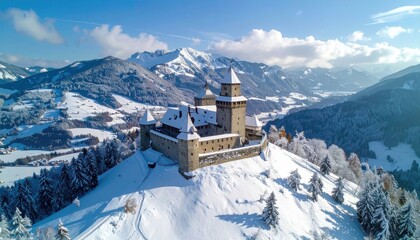 Snow Covered Medieval Castle on Hilltop against Mountain Range Under Blue Sky in Winter Landscape