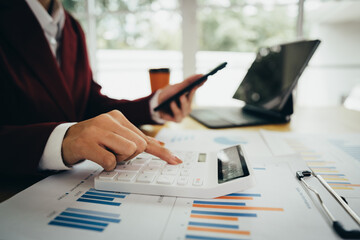 Business professional using tablet and laptop with financial charts and graphs on desk, analyzing business data and performance reports.