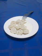 A Russian dish - a plate of vareniki with cottage cheese and sour cream on a table covered with a blue tablecloth