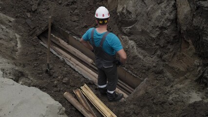 Construction worker inspects and measures deep trench for safety and precision. - Powered by Adobe