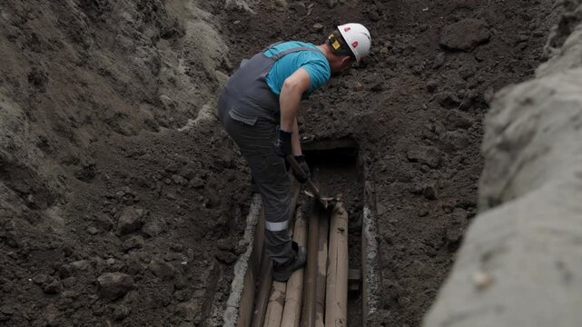 Worker digs in deep trench preparing underground pipeline installation.