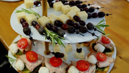 Multi level appetizer tray displaying skewered cheese, grapes, olives on upper tier, lower tier holding bruschetta topped with ham, mozzarella, tomato slices