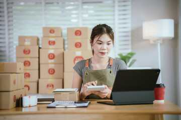 A young woman is packing a parcel with tape at a home office desk, surrounded by boxes, tablet, and coffee cup.