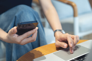 Woman using mobile phone and laptop computer remote working at coffee shop. Woman using smartphone for online shopping and internet banking via mobile app, social media networking