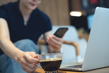 Young asian woman using smartphone, take a coffee break during remote working on laptop computer at coffee shop. Freelancer using mobile phone, online working at cafe, business casual
