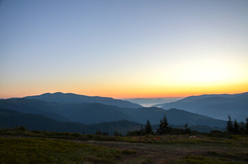 Peaceful view of layered mountains and trees at sunrise showcasing a warm and gentle glow. Carpathian Mountains, Ukraine