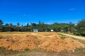 A football field under renovation with piles of soil and a clear blue sky in the background.