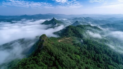 Aerial View of Lush Green Mountains Surrounded by Misty Clouds Under a Clear Blue Sky
