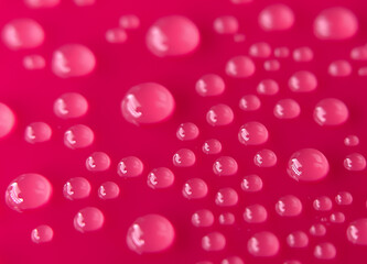 An abstract image of water droplets on a pink background. Concept: contrast and expressiveness, suitable for cosmetics advertising, textiles, and visual design. Macro photography.