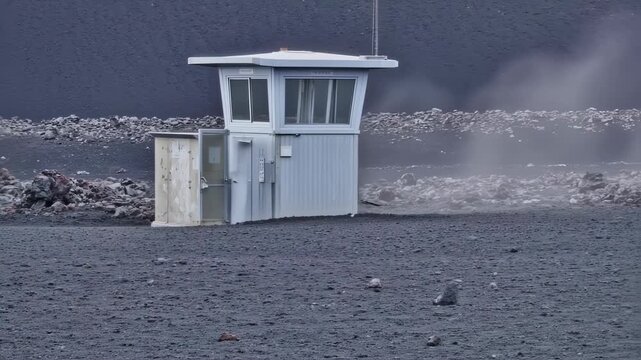 A light gray observation tower and support structures on dark volcanic terrain, with a hazy atmosphere