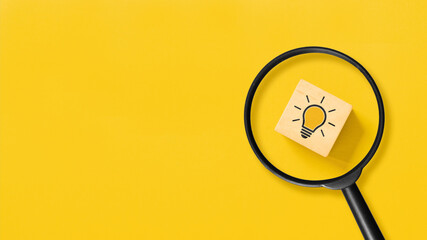Creative idea concept, magnifying glass and light bulb icon on wooden block with yellow background