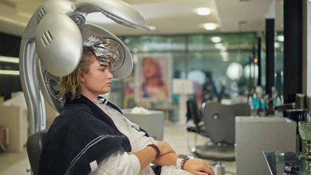 A woman sits under a climazone device in a hairdresser's salon. The latest technologies and hairdresser's assistants.