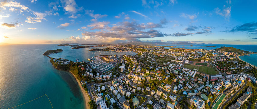 Fototapeta A stunning aerial panorama of Nouméa, the capital of New Caledonia, during a beautiful golden hour sunset. The city, marina, and turquoise bays are bathed in warm evening light