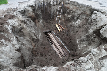 Deep excavation site with wooden beams and ladder for construction project.