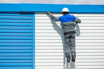 Worker Installing Panels on a Building Exterior Using a Ladder.