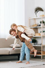Playful couple shares a joyful piggyback moment in a bright living room, capturing warmth, affection, and candid lifestyle happiness in a cozy home setting.
