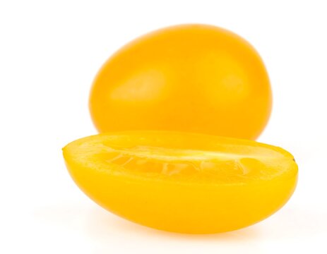 Two vibrant yellow cherry tomatoes, one whole and one halved, against a white background - Powered by Adobe