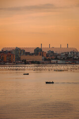 Boats floating under orange sky, with city and industrial background of Taranto
