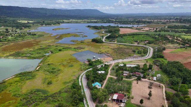 Drone footage of aerial view of Lam Phra Phloeng reservoir and surrounding farmland in Wang Nam Khiao, Nakhon ratchasima, Thailand. Scenic landscape of countryside with curved rural roads 