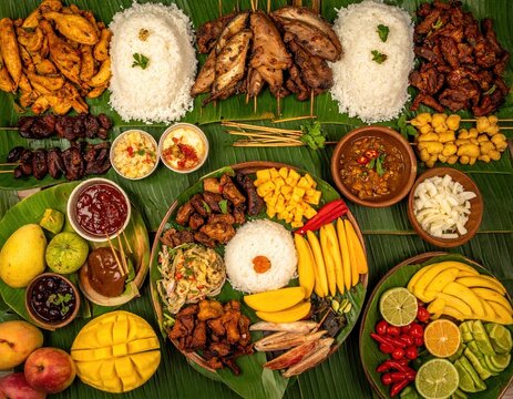 Overhead shot of filipino fiesta food platter featuring grilled meats rice and tropical fruits on banana leaves creating a vibrant cultural feast