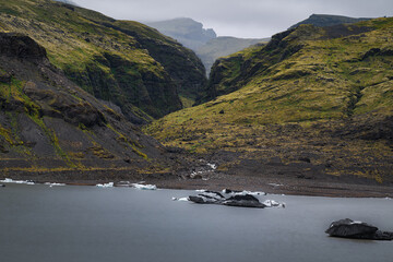 Black icebergs drift across a quiet lagoon