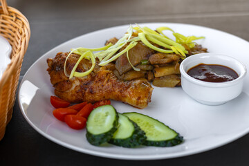 white plate with potatoes and onions, garnished with fresh leek. Side of sweet cherry tomato halves, cucumber slices and rich barbecue sauce 