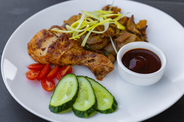 white plate with potatoes and onions, garnished with fresh leek. Side of sweet cherry tomato halves, cucumber slices and rich barbecue sauce 