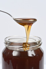 A spoonful of golden honey is dripping slowly into a jar of darker honey, creating a visual display...