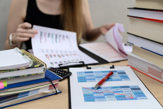 A busy woman sits at a desk surrounded by papers, binders, documents and books.