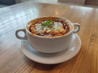 A delicious single-serving bowl of freshly oven-baked lasagna with melted cheese and rich tomato sauce, served on a wooden table