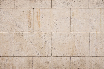 Textured beige stone wall with rectangular blocks arranged in a grid pattern, showcasing natural imperfections and subtle variations in color and texture, for backgrounds and architectural designs