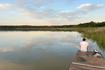 Fishermen catch fish from a wooden pier at sunset over a calm lake
