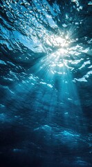 Sunbeams pierce deep blue ocean water, creating a dramatic underwater light show with textured surface and dark depths