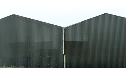 Industrial metal buildings with distinct angular roofs in a cloudy atmosphere during daytime,...