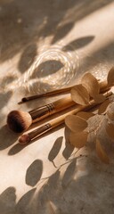 Three makeup brushes with golden handles rest on a light-colored surface, adorned with dried eucalyptus leaves, bathed in warm sunlight casting dramatic shadows